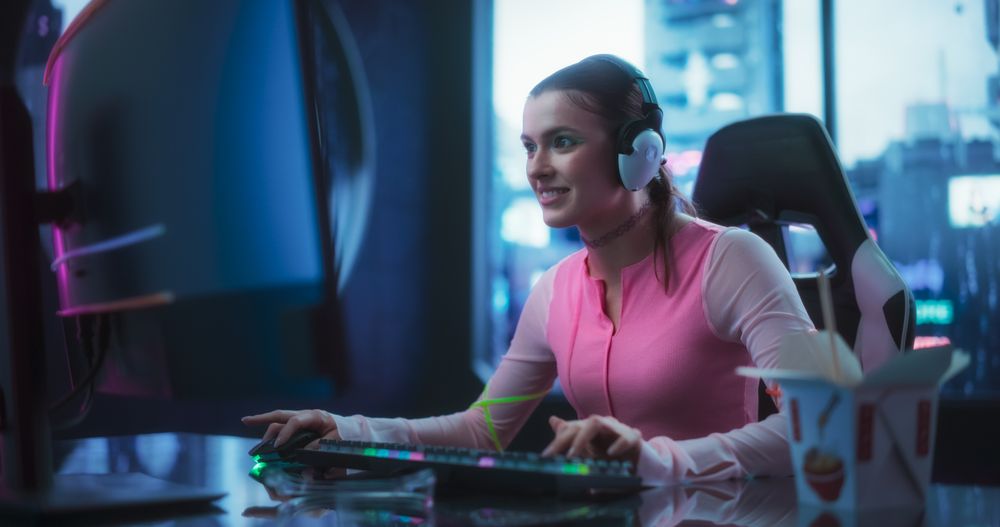 Young Woman Wearing Futuristic Clothes, Bright Green Makeup and Neon Rings, Playing Video Games on a Desktop Computer.