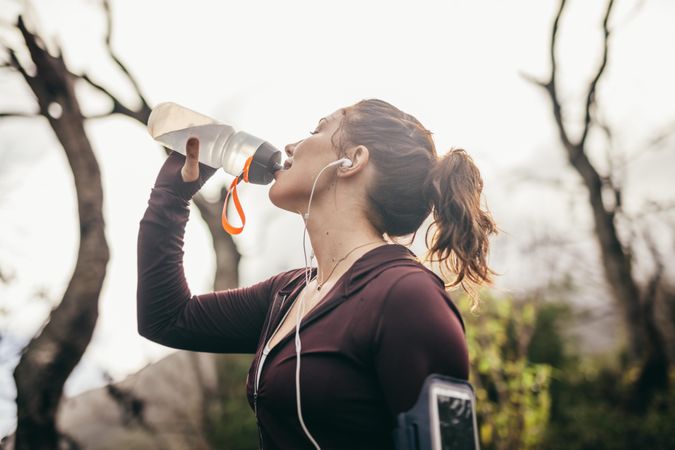 Female runner taking a break and drinking water from bottle in morning