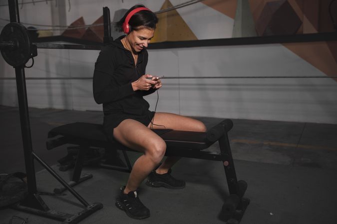 Woman with headphones and device sitting in gym