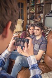 Friend taking photos to cute couple on a sofa