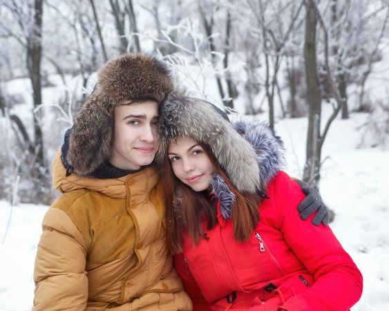 Loving teenage boy and girl sitting in snowy forest with arms around each other