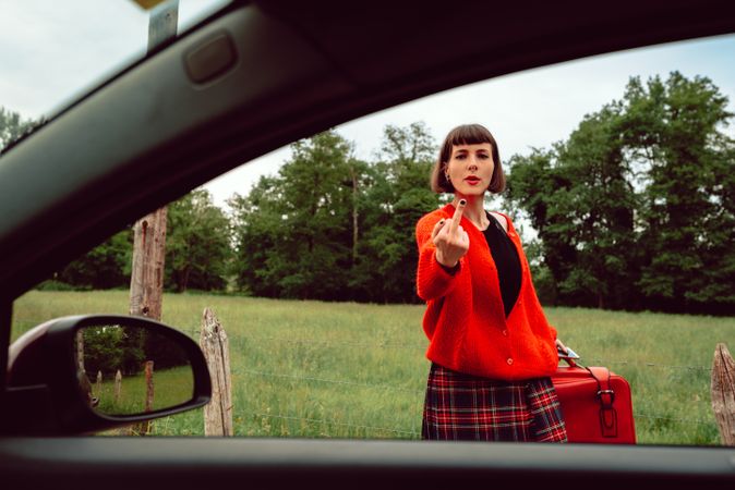 Woman in red sweater gesturing near car on road