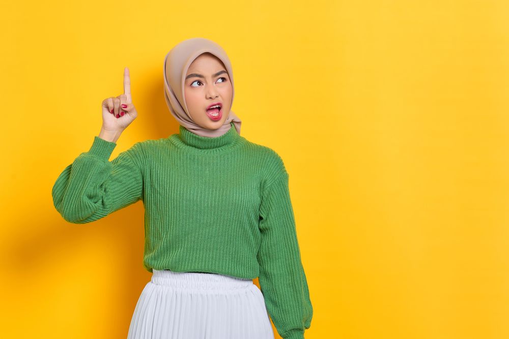 Surprised woman in headscarf holding up finger while holding on phone