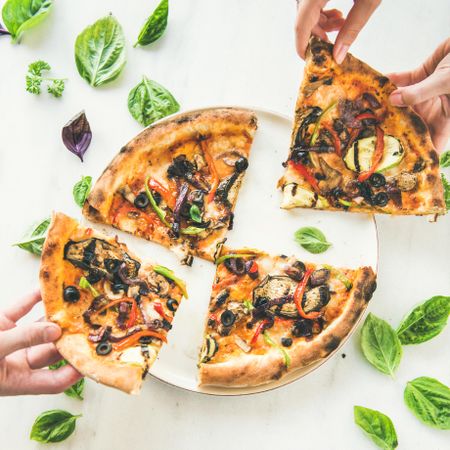 Quartered wood fired vegetable pizza with hands taking slices