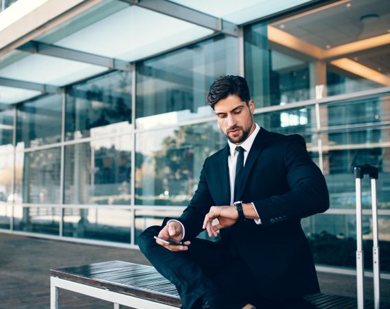 Young businessman waiting and checking time with mobile phone