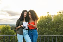 two young women smiling and using her mobiles on a terrace. with the sunset
