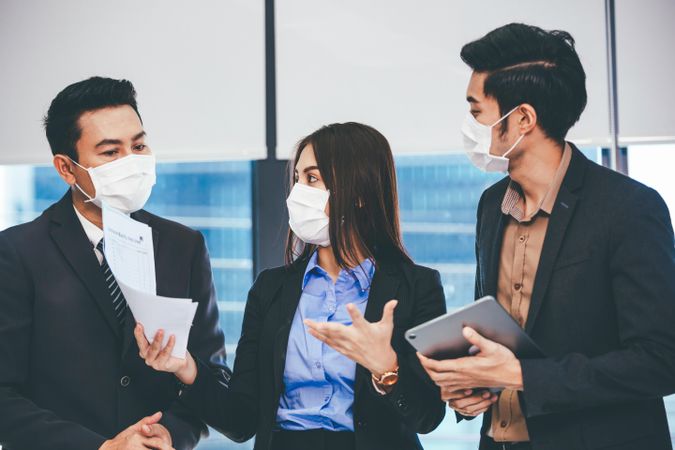 Asian office workers discussing project together wearing facemasks