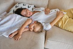 Woman and daughter resting on sofa in apartment