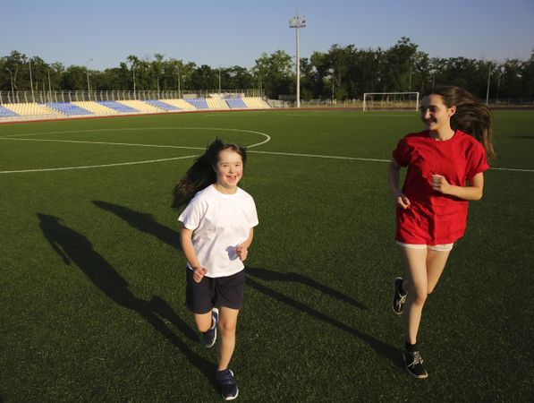 Two siblings running along soccer field together