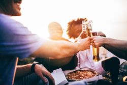 Group of friends toasting over beers, and pizza at sunset