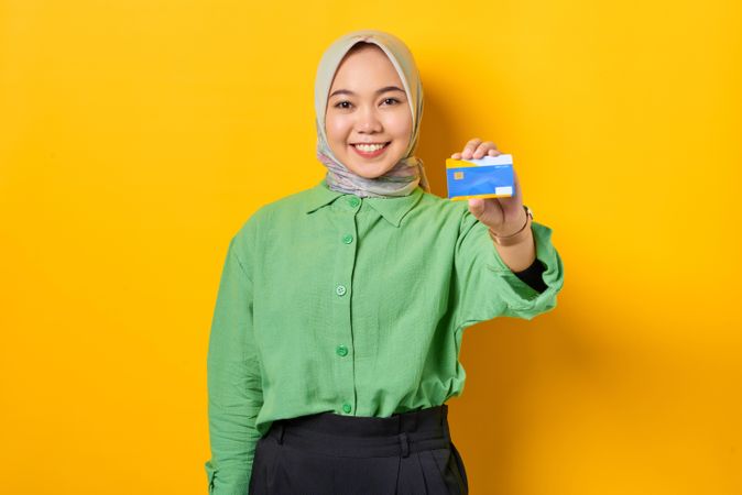 Smiling Muslim woman in headscarf and green blouse holding up credit card