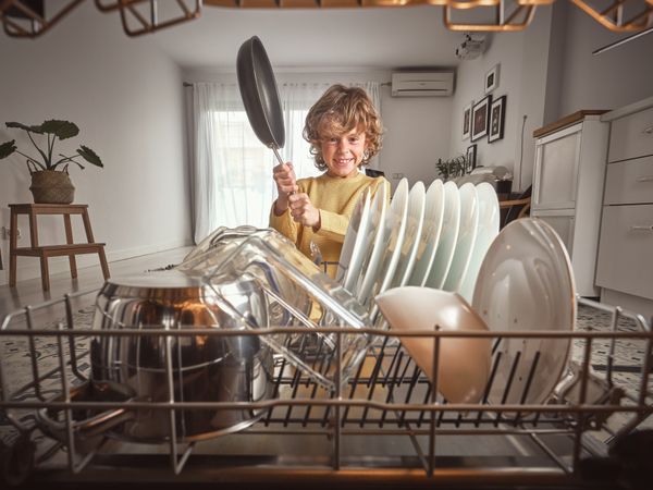 Positive boy with frying pan near dishwasher