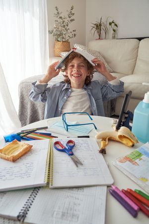 Cheerful boy covering head with copybook and smiling