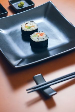 Two sushi rolls on plate next to chopsticks ready to eat at restaurant