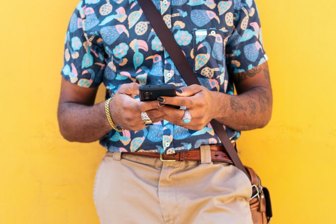 Stylish Black man using smartphone outdoors over yellow background
