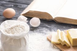 Bag of wheat flour, butter and eggs, on a wooden table and open book