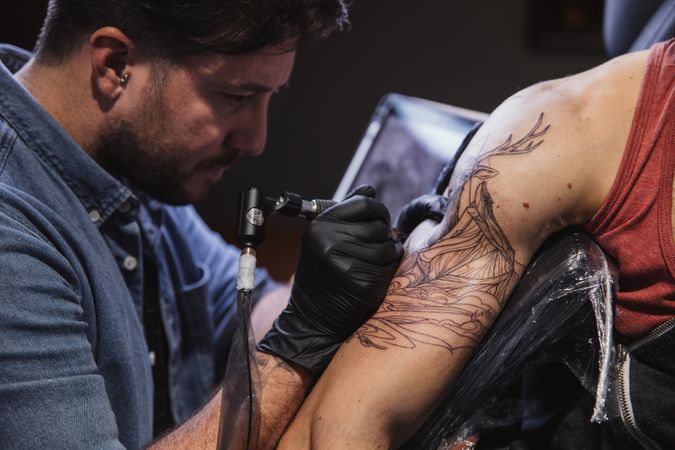 Master doing tattoo on forearm of male customer