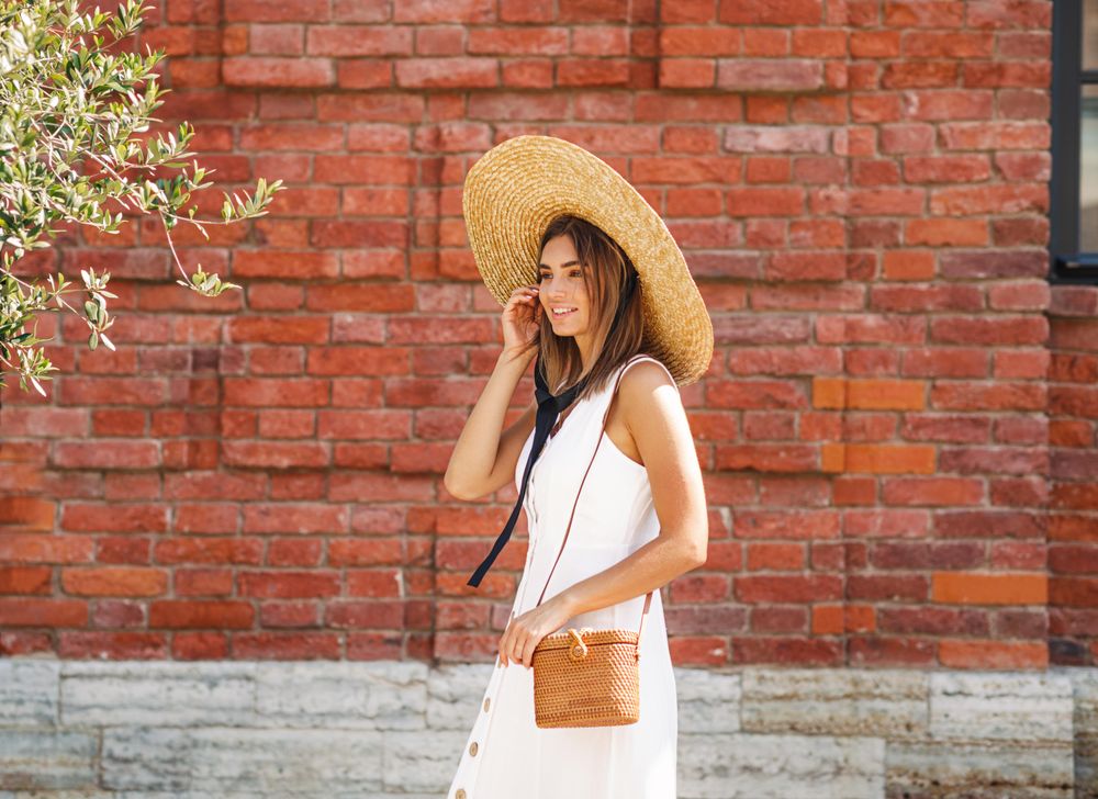 Woman in summer dress & straw hat standing in front of a red brick building