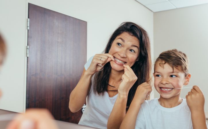 Little boy with his mother in bathroom cleaning teeth with dental floss