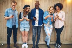Multi-ethnic group of friends standing against a wooden fence sharing content on their phones