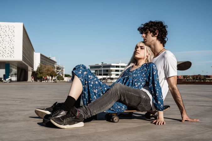 Trendy couple sitting together on skateboard on street