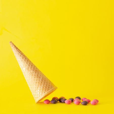Upside down ice cream cone with candy on yellow background