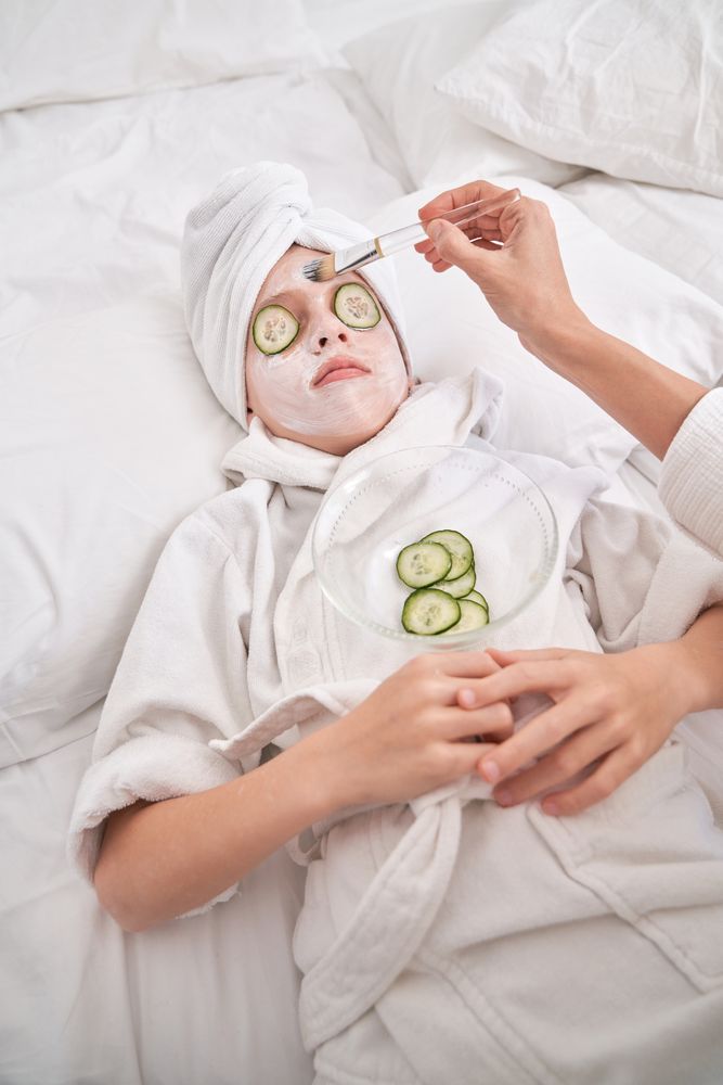 Unrecognizable mother applying mask on face of child during spa