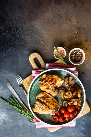 Top view of plate of grilled chicken with tomatoes and mushroom on counter with copy space