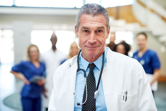 Portrait of mature doctor in lab coat and stethoscope with his team in the background