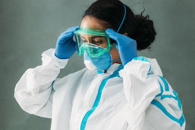 Side view of Black female medical professional in PPE gear adjusting her googles