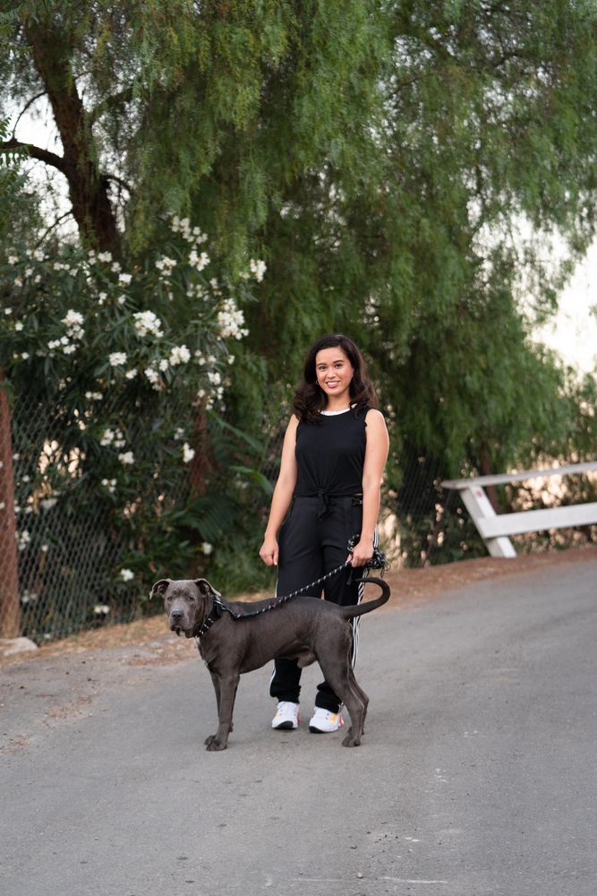 Woman posing in an open street   in front of trees with her dog