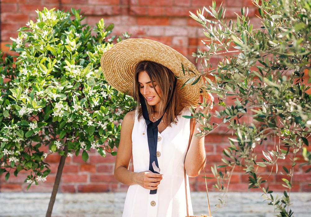 Woman standing between two bushes in front of brick building
