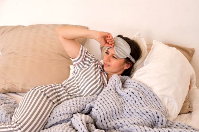Woman feeling discomfort in bed with eye mask.