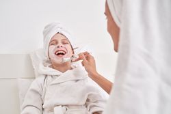 Woman smearing cream mask on face of laughing kid