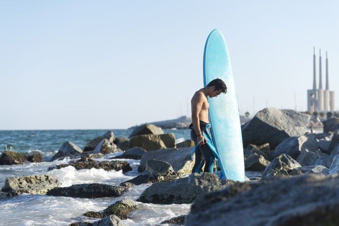 Male surfer with blue board standing in the sea around a rocky coast