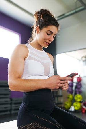 Woman looking down at her smart phone in gym, vertical