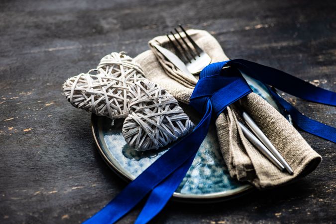 Blue ribbon wrapping cutlery with heart decorations on plate