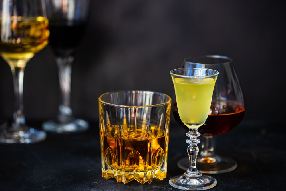 Side view of glasses of different spirits on dark background