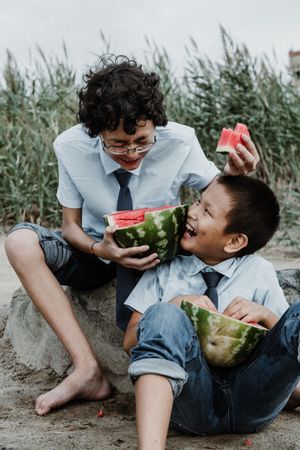 Teen boys playing while eating watermelon on beach