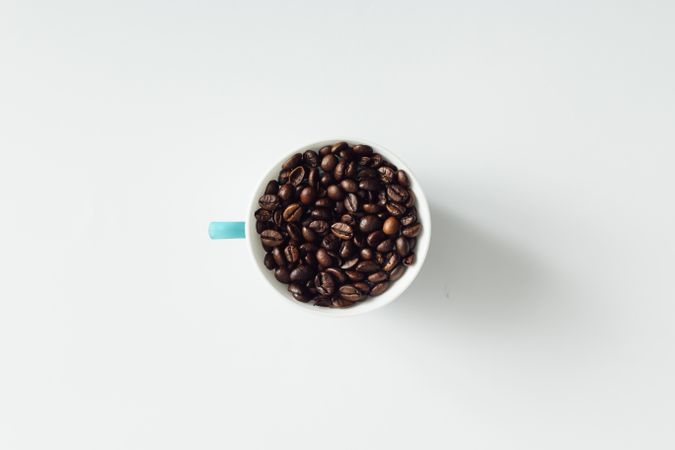 Coffee cup filled with coffee beans on light background