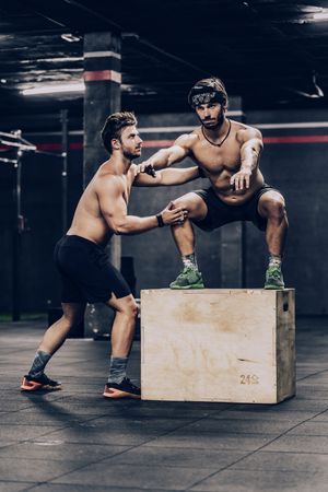 Muscular fellows doing workout and squatting in sport club