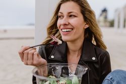 Content woman eating salad from plastic bowl sitting on wooden terrace
