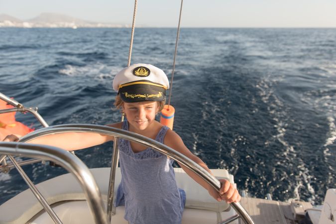 Smiling girl holding steering wheel on yacht on water