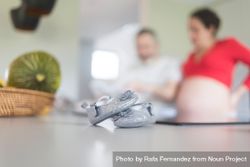 Silver baby shoes in foreground of pregnant woman with man bGpxe0