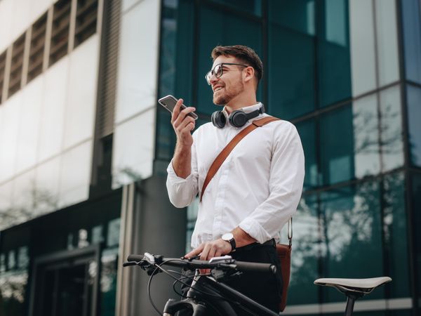 Man holding his bicycle and talking over mobile phone while walking to office