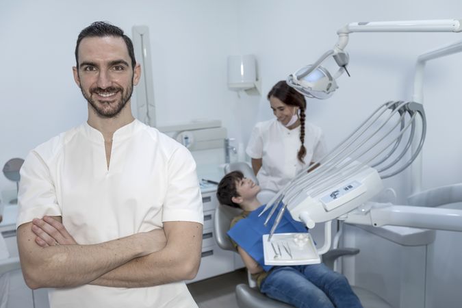 A portrait of a happy dentist with smiling teenage patient sitting in the background