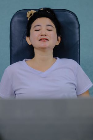 close up of a woman wearing a light white V-neck dress, sitting on a dark gray chair