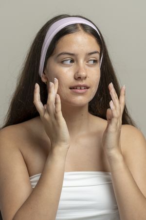 Young woman applying facial scrub cream on natural skin texture in bright home studio