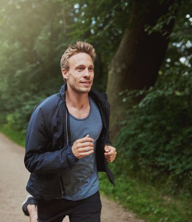 Athletic confident man in sporty vest & windbreaker jogging outdoors