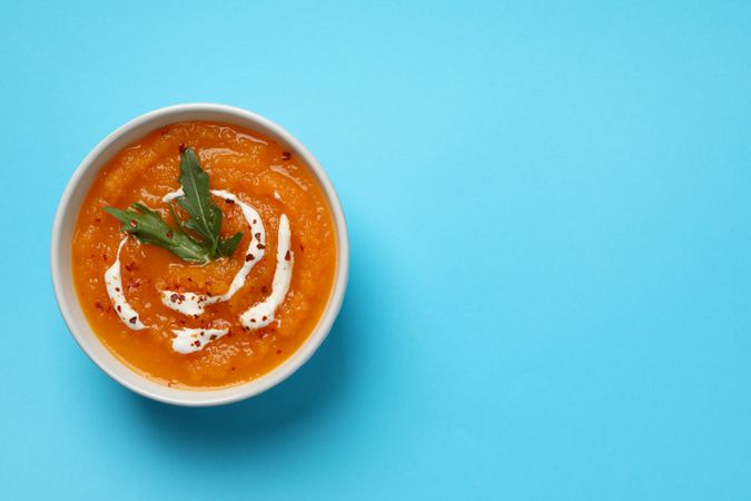 Top view of bowl of pumpkin soup on blue table, copy space
